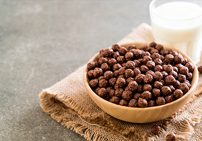 a bowl of chocolate breakfast cereal on a hessian tarp next to a glass of milk